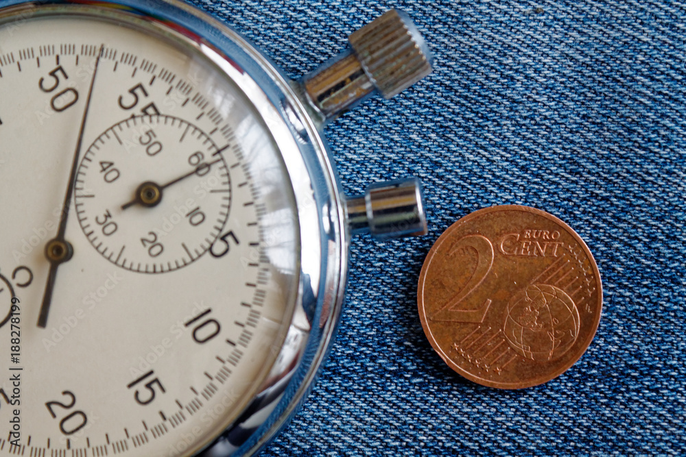 Euro coin with a denomination of 2 euro cents and stopwatch on worn blue denim backdrop - business background