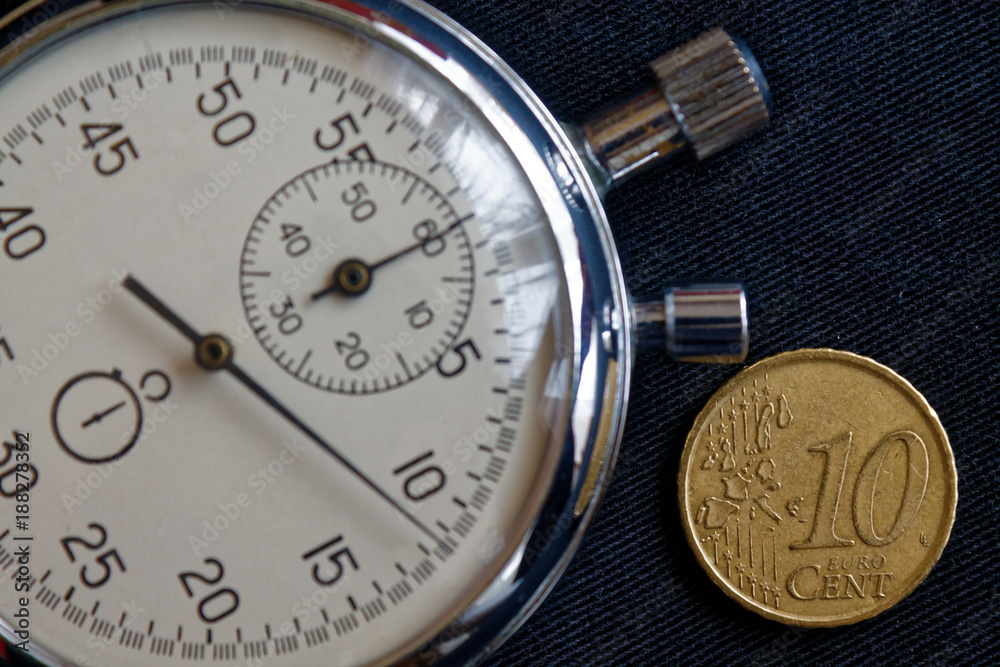 Euro coin with a denomination of 10 euro cents and stopwatch on black denim backdrop - business background Euro coin with a denomination of 10 euro cents and stopwatch on black denim backdrop - business background