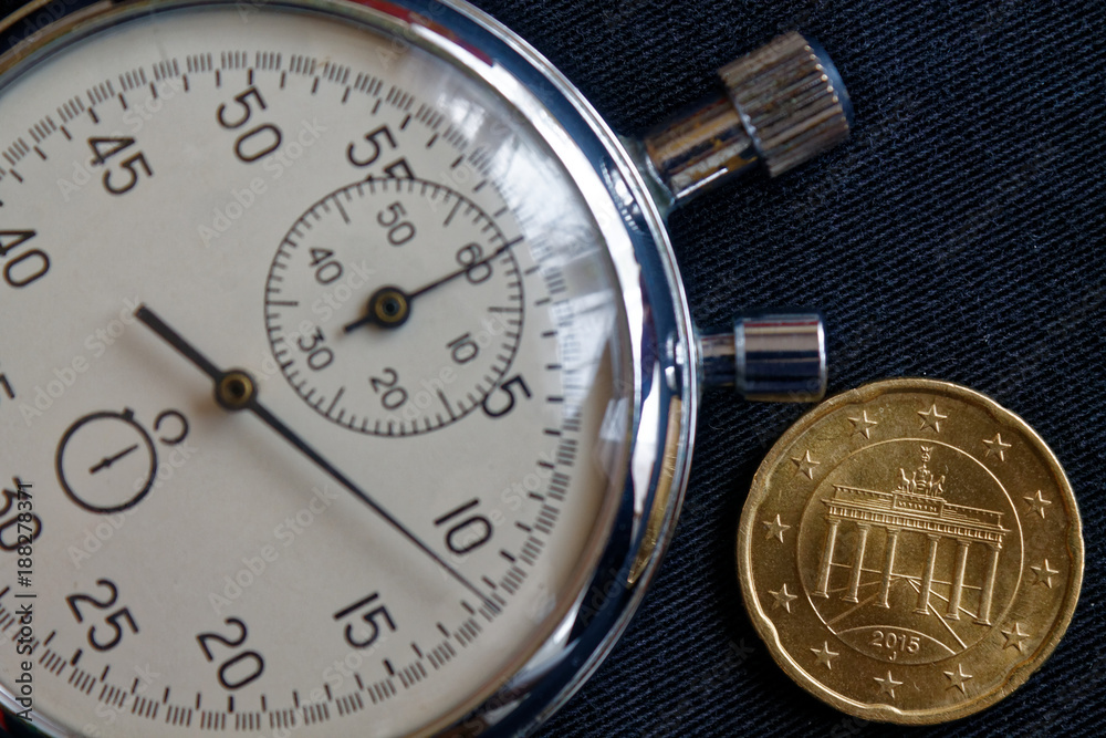 Euro coin with a denomination of twenty euro cents (back side) and stopwatch on worn black denim backdrop - business background Euro coin with a denomination of twenty euro cents (back side) and stopwatch on worn black denim backdrop - business background
