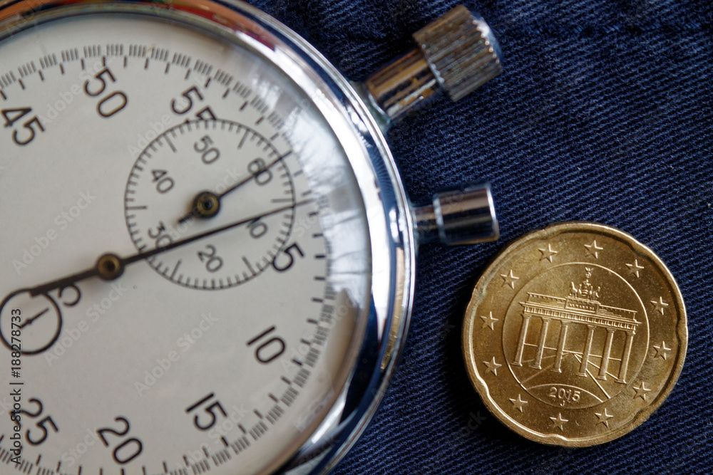 Euro coin with a denomination of twenty euro cents (back side) and stopwatch on worn blue jeans backdrop - business background Euro coin with a denomination of twenty euro cents (back side) and stopwatch on worn blue jeans backdrop - business background