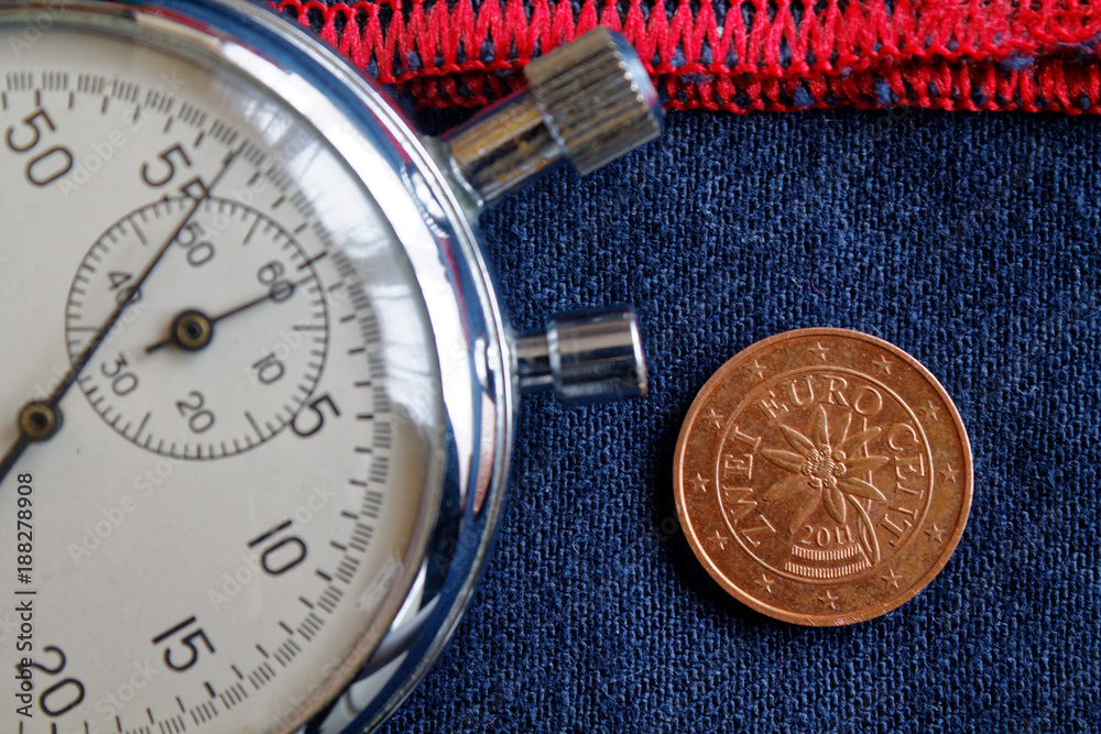 Euro coin with a denomination of two euro cents (back side) and stopwatch on worn blue denim with red stripe backdrop - business background