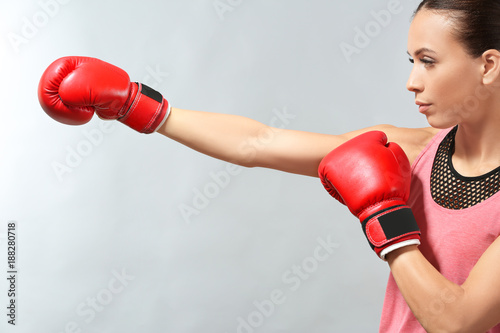 Strong woman in boxing gloves on grey background © Africa Studio