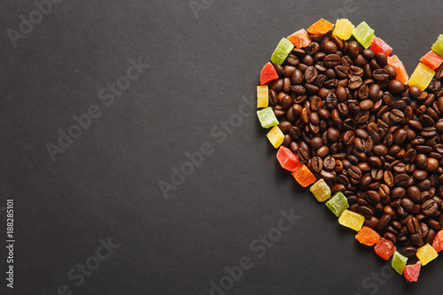 Colorful candied fruits in the form of heart with brown coffee beans isolated on black background for design. Saint Valentine's Day card on fabruary 14, holiday concept. Copy space for advertisement.