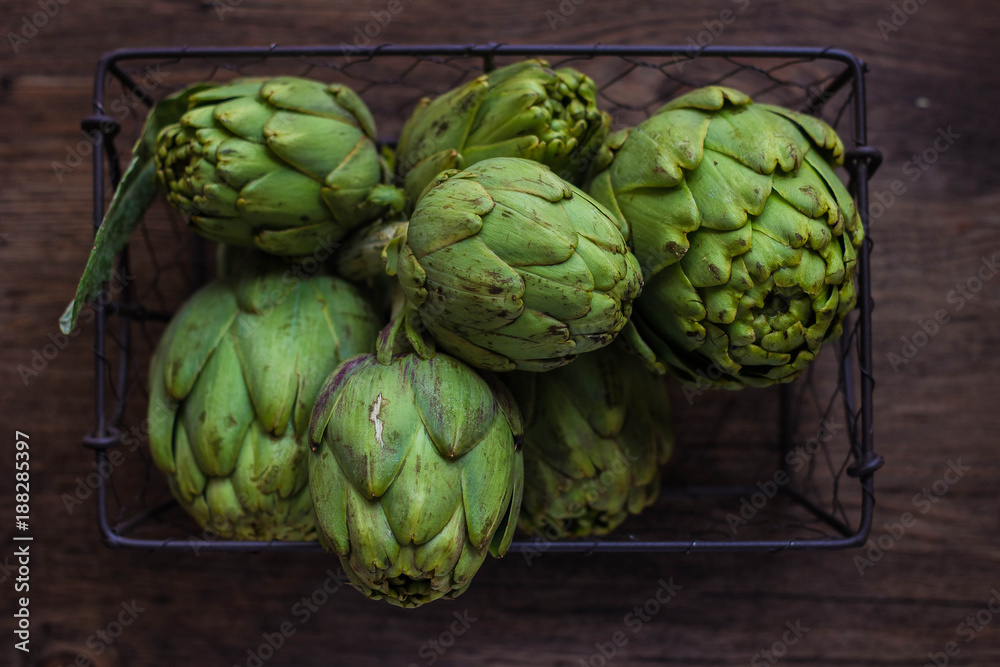 Fresh organic artichokes over a dark blue napkin with knife and lemon and with metal basket with artichokes over a rustic wooden background. Top View Fresh organic artichokes over a dark blue napkin with knife and lemon and with metal basket with artichokes over a rustic wooden background. Top View