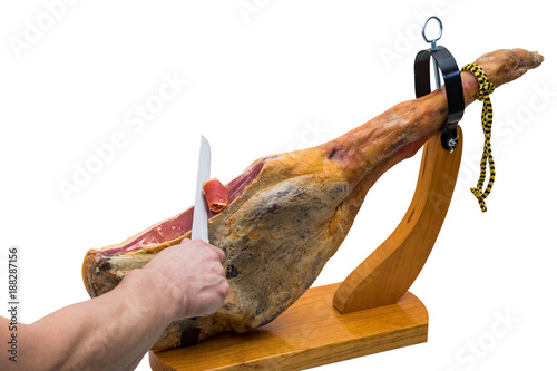 Hand cuts with knife at a spanish serrano ham in a wood - holder - isolated