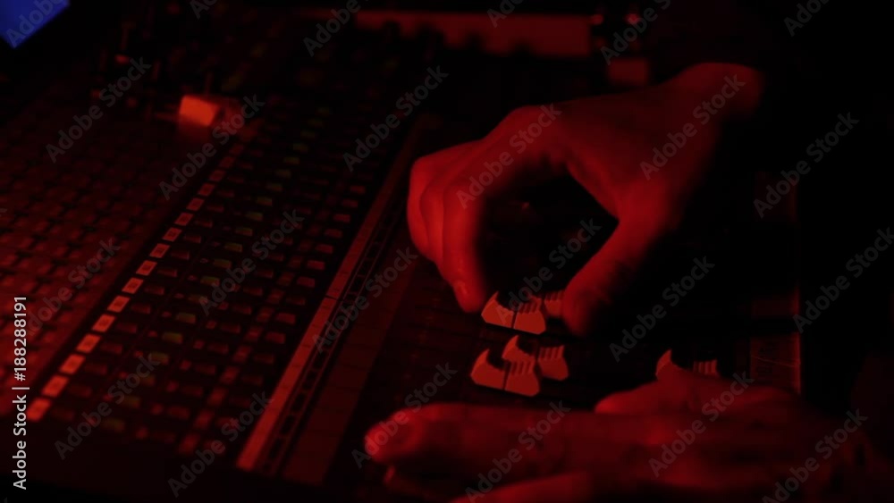 Manos ajustando niveles en mesa de control de audio en concierto de musica y luces en color rojo