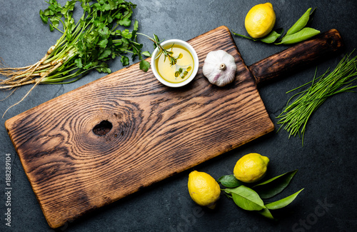 Herbs - spreeng onion, lemons, coriander, garlic rosemary and oil arount wooden cutting board, top view, copy space. Cooking, food background photo