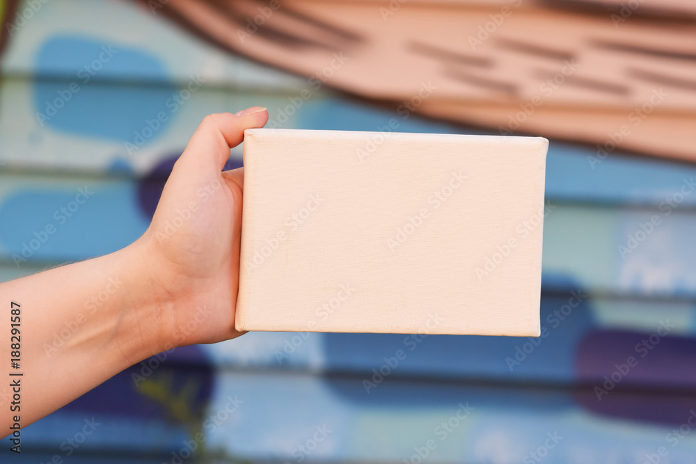 Female hand with tiny canvas in front of urban background Female hand with tiny canvas in front of urban background