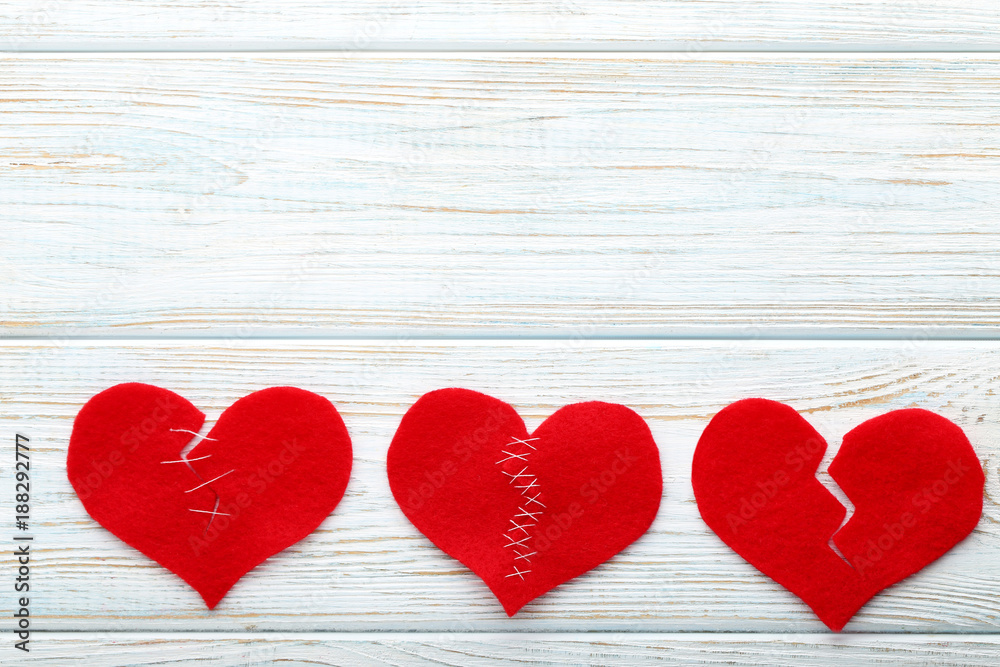 Broken red hearts on white wooden table Broken red hearts on white wooden table