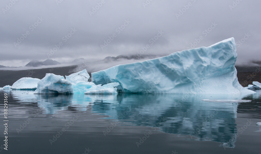blue iceberg with perfect reflection in the fjord with dramatic mood of the sky