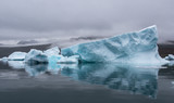 blue iceberg with perfect reflection in the fjord with dramatic mood of the sky