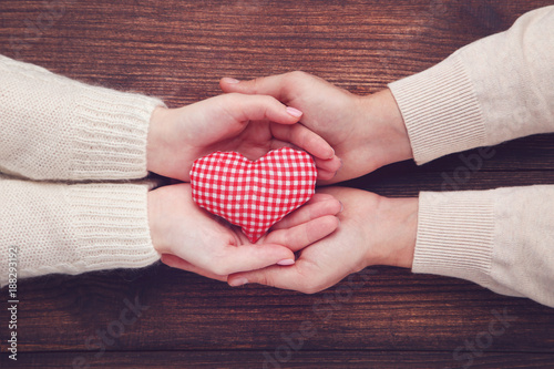 Female and male hand holding red fabric heart on brown background
