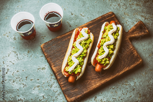 Chilean Completo Italiano. Hot dog sandwiches with tomato, avocado and mayonnaise served on wooden board with drink in paper cup . Top view. Independence Day concept