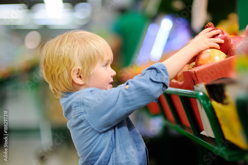 Cute little boy in a food store or a supermarket choosing fresh organic pomegranate
