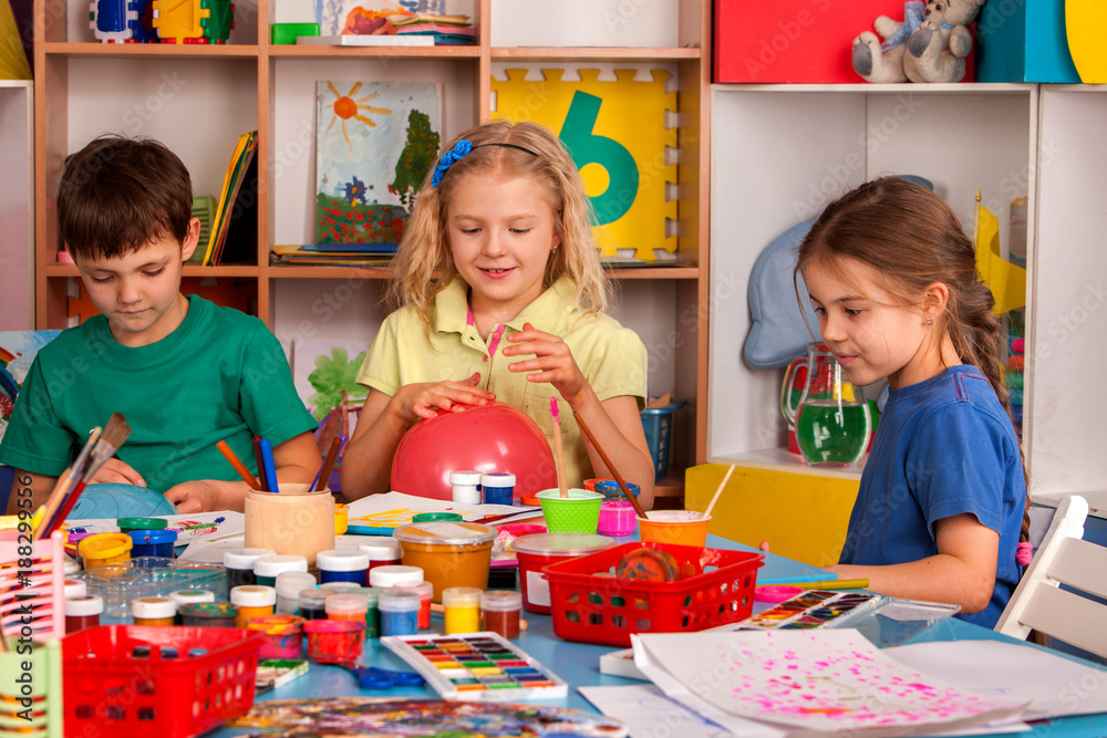 Naklejka premium Small students with teacher finger painting in art school class. Teacher cheers children in kindergarten. Newcomer in children's team. Craft drawing education develops creative abilities of children.