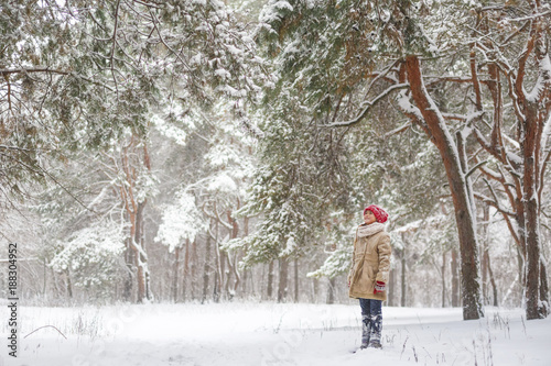 Beautiful little girl have fun in snowy winter forest. Adorable child wearing a red knitted hat and jacket walk outdoor at Christmas. Kid playing in snowy forest. Family winter vacation in mountains