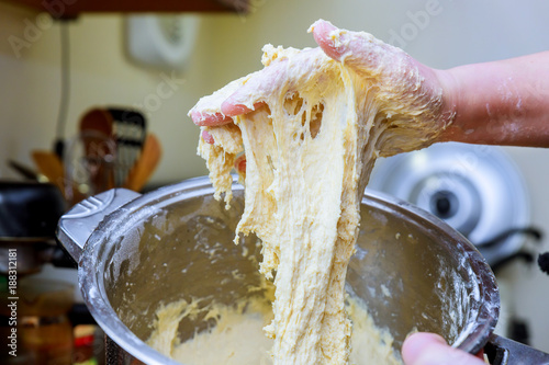 Cropped shot of hands knead dough on table, surrounded with much flour, bowls, eggs and milk. Professional chef works in bakery, preapares delicious photo