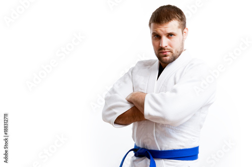 Young sporty man with dark hair in a white kimono with blue belt for sambo, jiu jitsu, judo posing on white isolated background © Виталий Сова