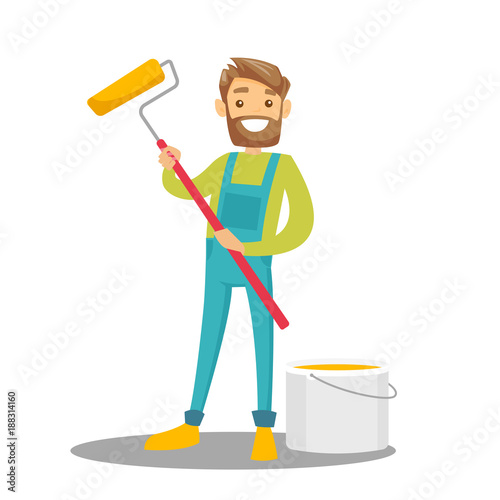 Young cheerful caucasian white hipster painter in uniform holding a paint roller in hand while standing near the bucket with yellow paint. Vector cartoon illustration isolated on white background.