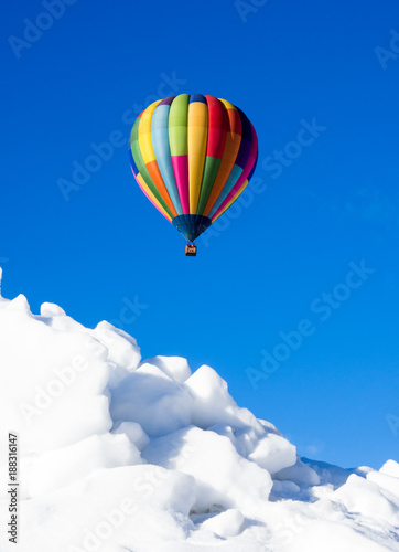 Colorful hot air balloon flying over snowy field in winter