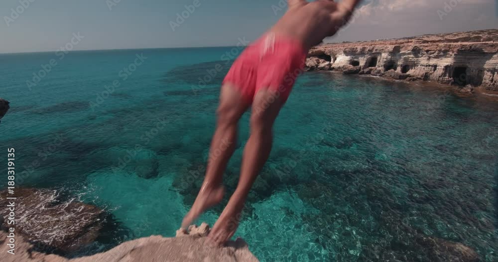 Man doing somersault jumping off cliff and diving into sea
