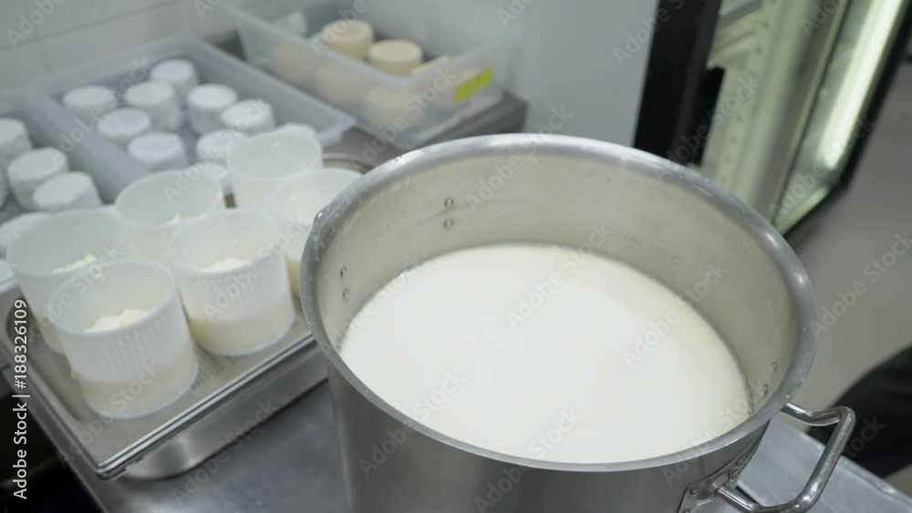 The round white and yellow cheese is being prodcted in industrial manufacture. The wheels of food are in the storage on the plant. The man in gloves opens tank with fresh milk - traditional ingredient