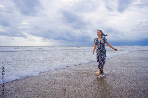 portrait of young beautiful and happy Asian Chinese woman on her 20s or 30s wearing long chic dress walking alone on beach sea water enjoying