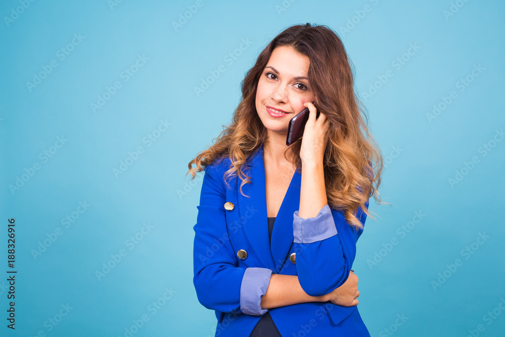 Fototapeta premium Smiling woman talking on the smart phone on blue background