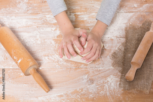 hands of a girl kneading dough and rolling out on a wooden board