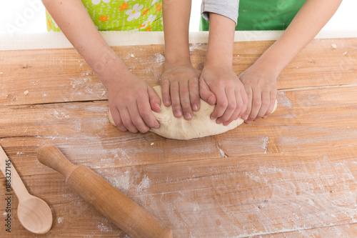 hands of children, boy and girl knead the dough on a wooden board