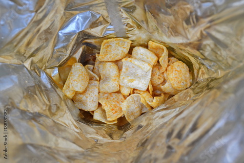 Fried potato golden chips with hot red pepper on bottom of the foil packaging. Texture. Background