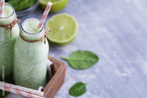 Two spinach smoothies with lime in the glass bottles with straws