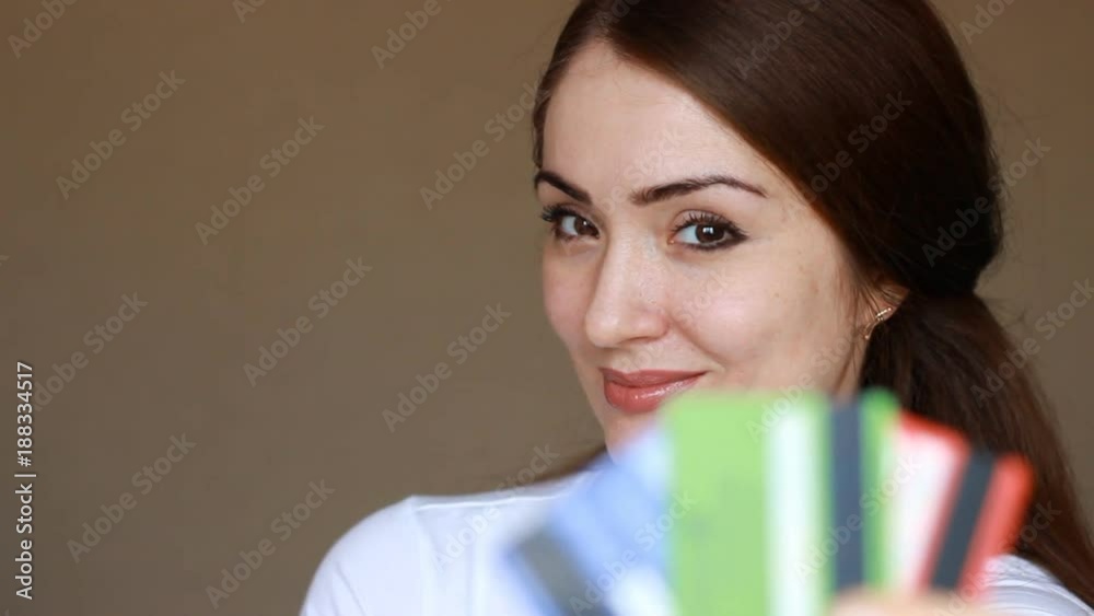 Portrait of a young beautiful woman close-up, who is smiling, looking at the camera and holding credit bank cards of different colors and banks. The concept of choosing and saving credit, finance, and Portrait of a young beautiful woman close-up, who is smiling, looking at the camera and holding credit bank cards of different colors and banks. The concept of choosing and saving credit, finance, and
