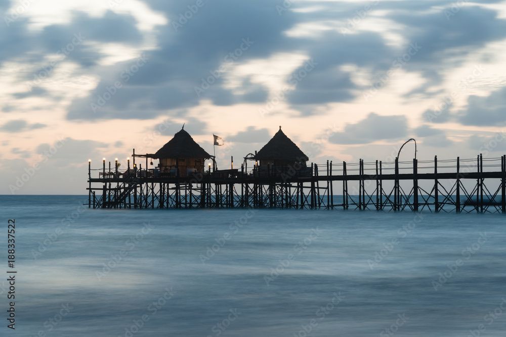 Wooden pier and thatched roofs on a tropical beach at sunrise, Zanzibar island