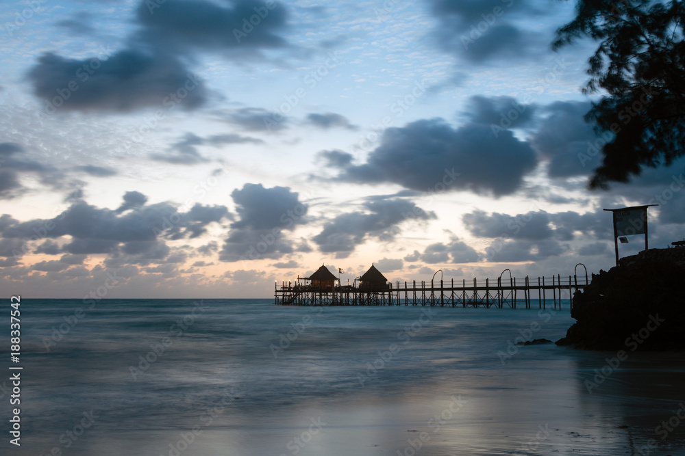 Wooden pier and thatched roofs on a tropical beach at sunrise, Zanzibar island