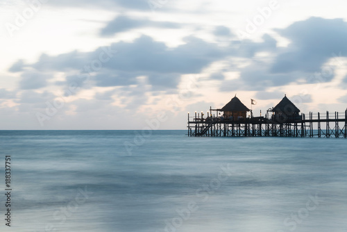 Wooden pier and thatched roofs on a tropical beach at sunrise  Zanzibar island