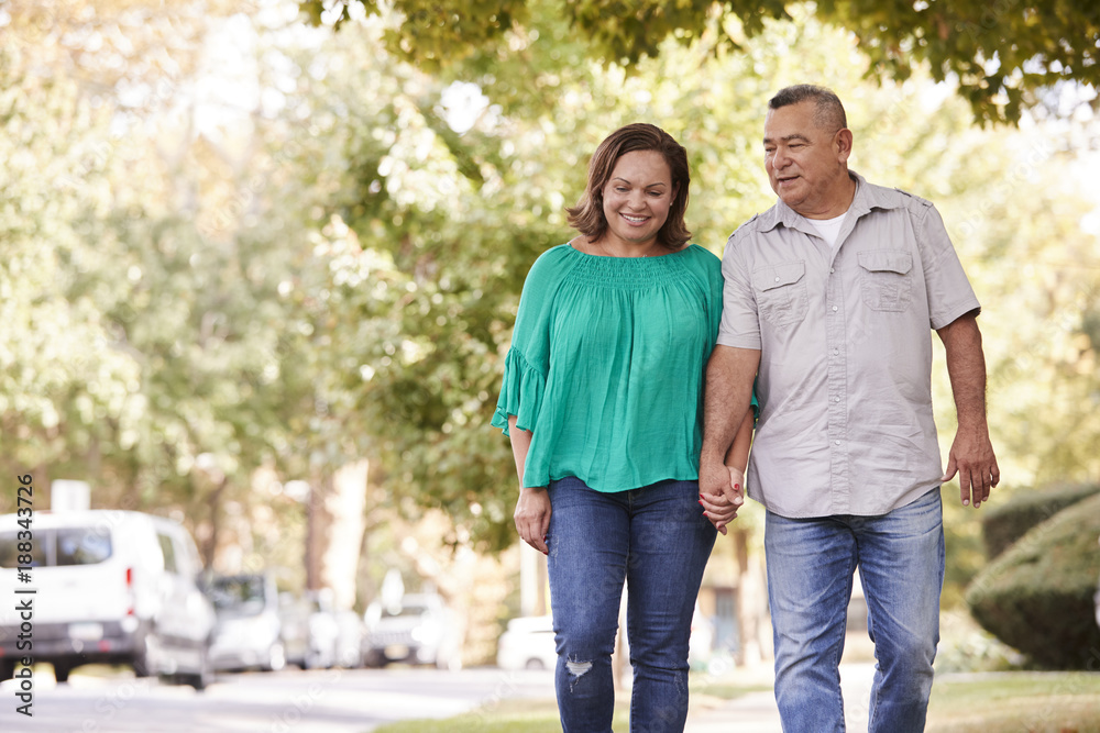 Senior Couple Walking Along Suburban Street Holding Hands