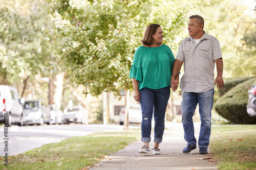 Senior Couple Walking Along Suburban Street Holding Hands photo