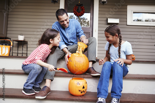 Фотография Father And Daughters Carving Halloween Pumpkin On House Steps