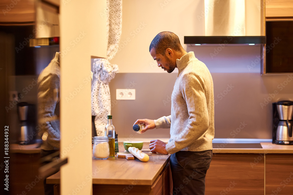 A serious handsome young man cooking in the kitchen in a sweater. A serious handsome young man cooking in the kitchen in a sweater.