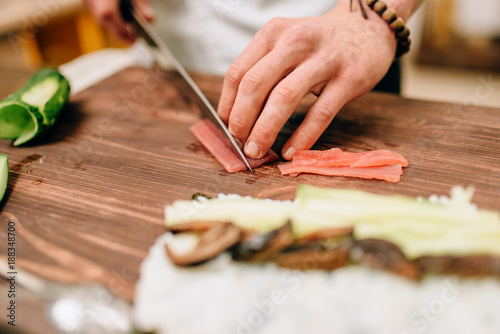 Male cook making sushi on wooden table, asian food
