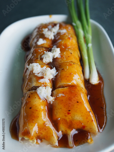 Thai local traditional street food, cut fresh spring roll, egg, tofu, bean sprout, sausage filling, black soy sauce salt gravy, decorated white crab meat, green spring onion, white plate, vertical