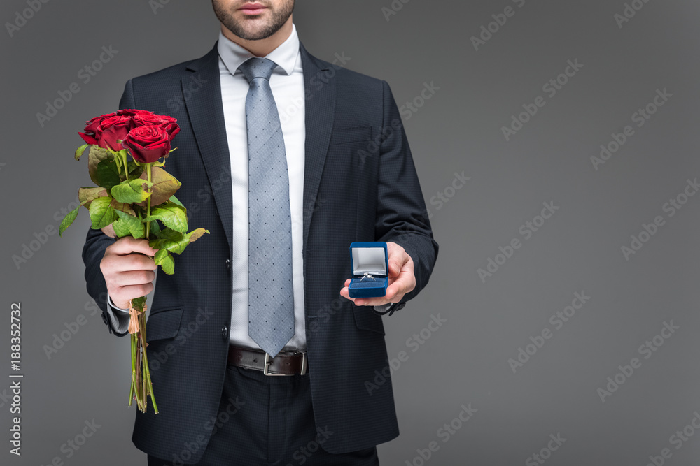 cropped view of man holding bouquet of red roses and proposal ring, isolated on grey cropped view of man holding bouquet of red roses and proposal ring, isolated on grey