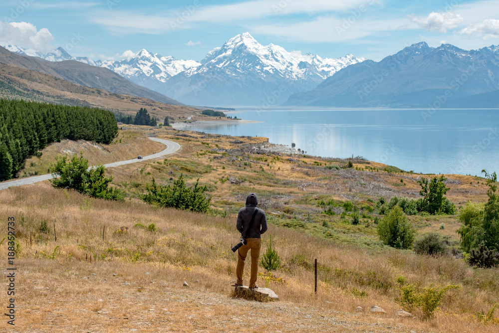 Young male photographer in hoody watching at Mount Cook, one of the most famous snowy mountain at peter’s lookout in South Island, New Zealand. Travel in summer concept