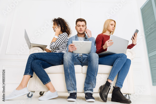 Cozy sofa. Confident girls using their gadgets and being attentive while sitting near their partner