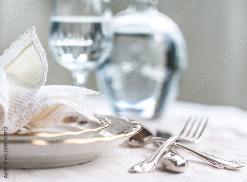Luxyry dinner set arranged on a table with vintage lace tablecloth and napkins, elegant porcelain dishes, silverware and crystal glassware