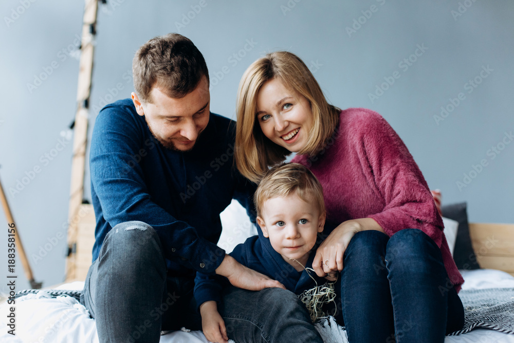 Cheerful parents and little boy sit on the bed in a cosy room Cheerful parents and little boy sit on the bed in a cosy room