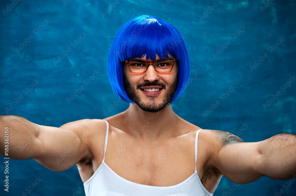 Transsexual person wearing blue wig and glasses posing on blue background