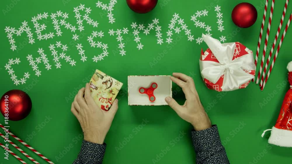 Adult man opening Xmas present box with fidget spinner inside on table with chroma key, top down shot