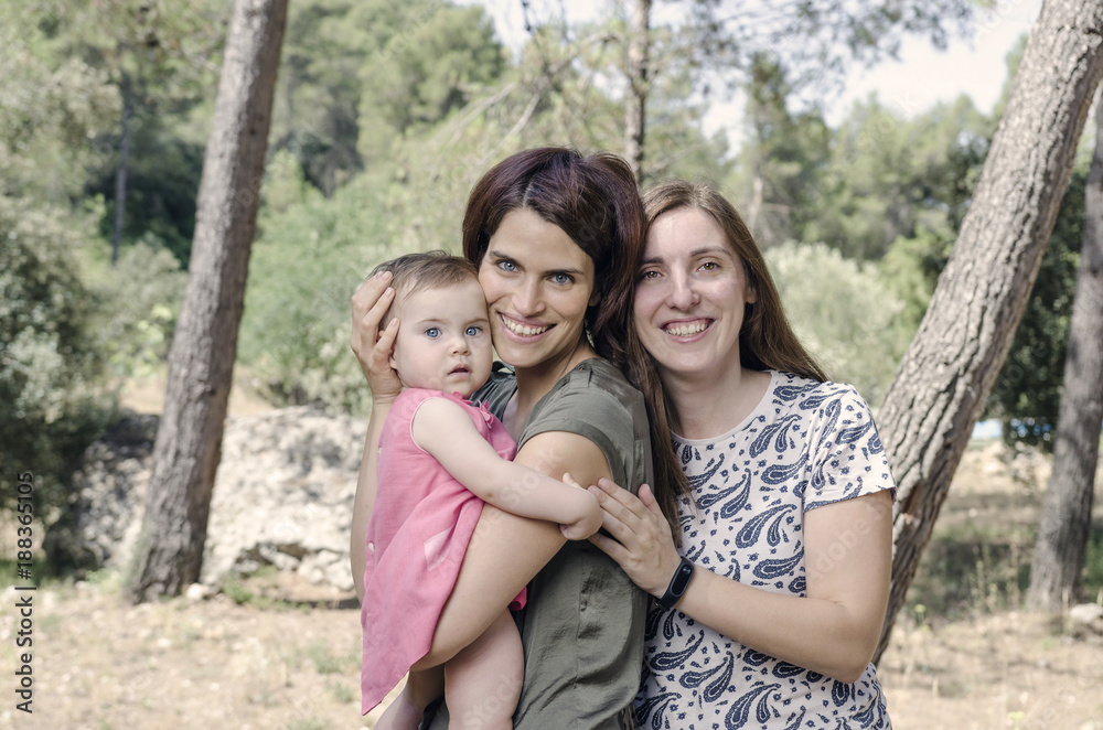 Portrait of happy lesbians mothers with a baby. Homosexual family in a countryside. Portrait of happy lesbians mothers with a baby. Homosexual family in a countryside.